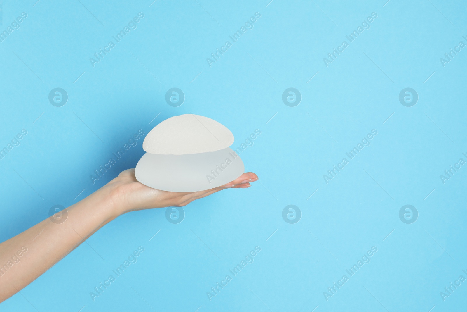 Photo of Woman holding silicone implants for breast augmentation on color background, space for text. Cosmetic surgery