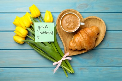 Photo of Cup of aromatic coffee with croissant, beautiful yellow tulips and Good Morning note on light blue wooden table, flat lay
