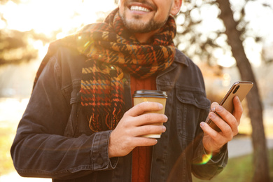 Man with cup of coffee and smartphone in morning outdoors, closeup
