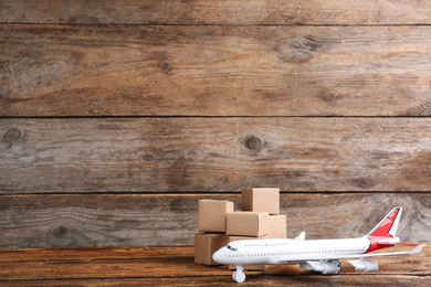 Photo of Airplane model and carton boxes on wooden background, space for text. Courier service