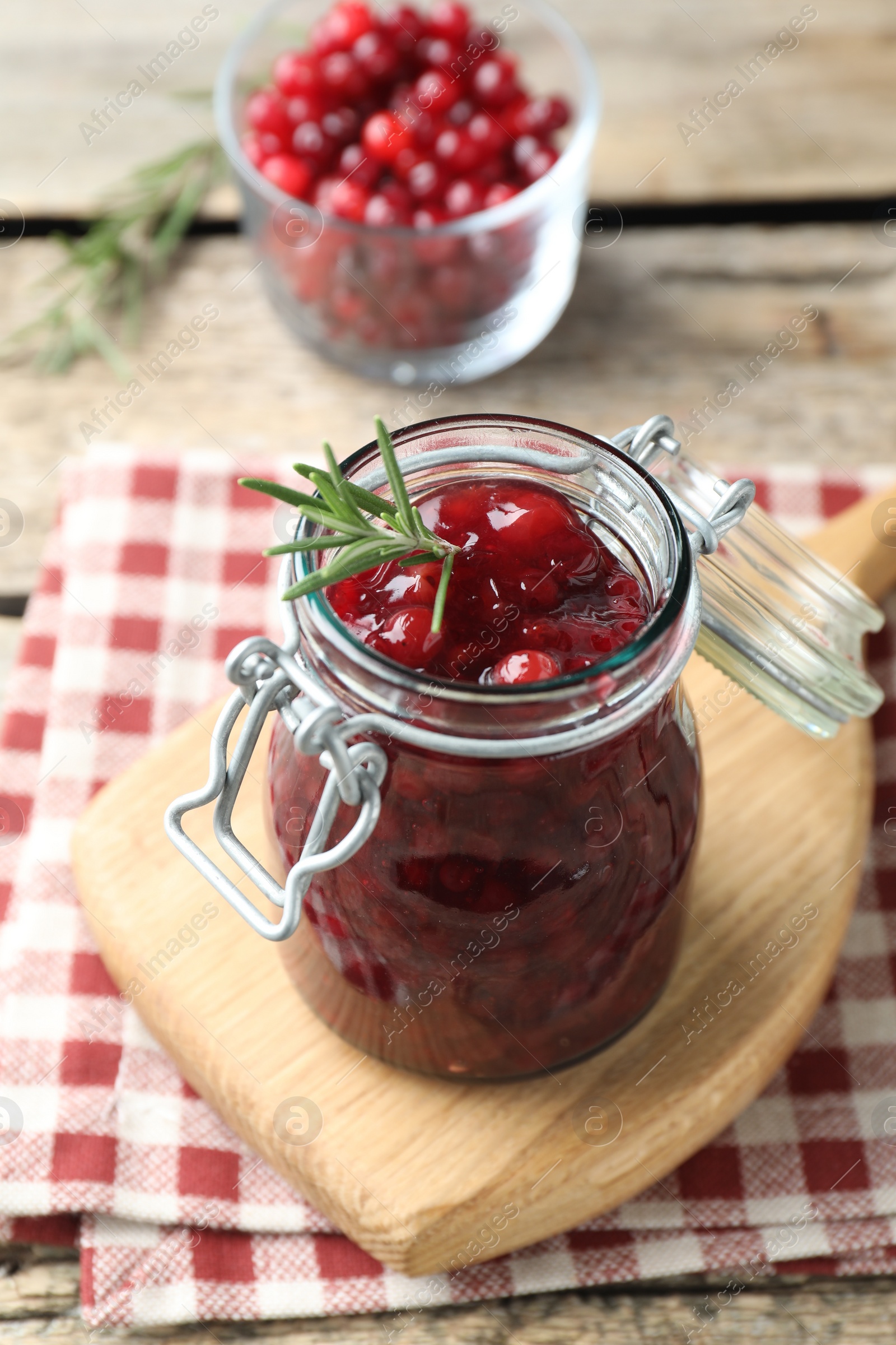 Photo of Fresh cranberry sauce in glass jar and rosemary on light wooden table