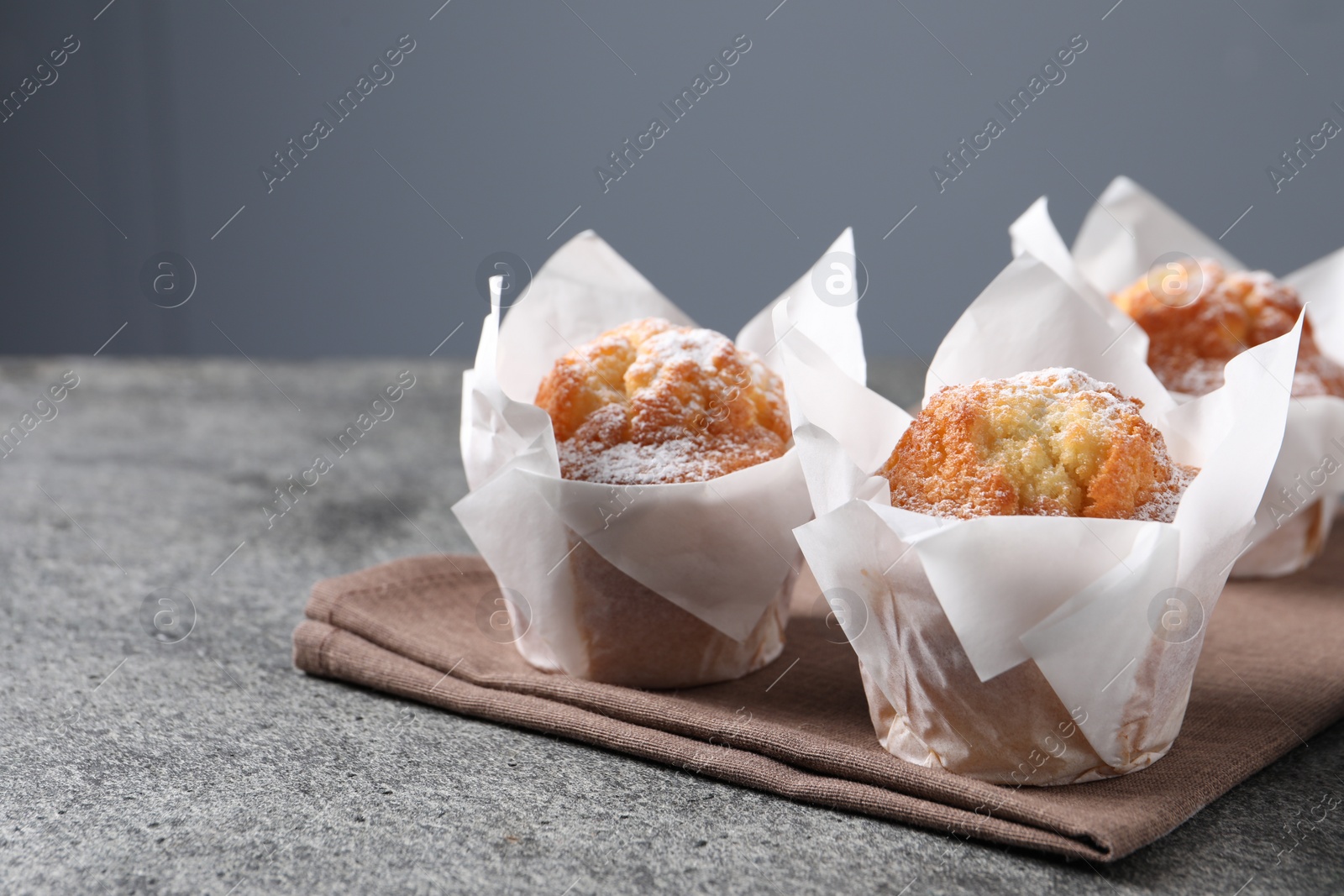 Photo of Delicious muffins with powdered sugar on grey table, closeup