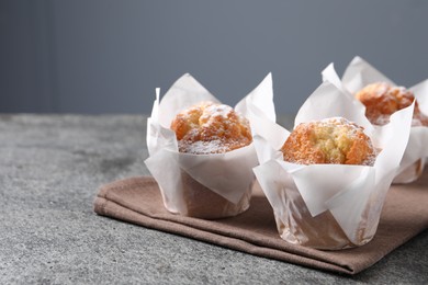 Delicious muffins with powdered sugar on grey table, closeup