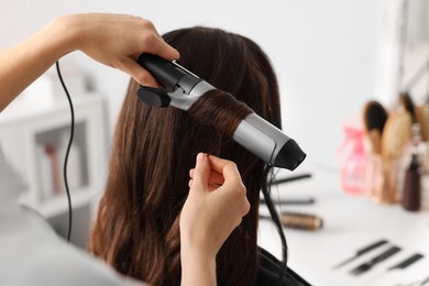 Photo of Hairdresser working with client using curling hair iron in salon, closeup