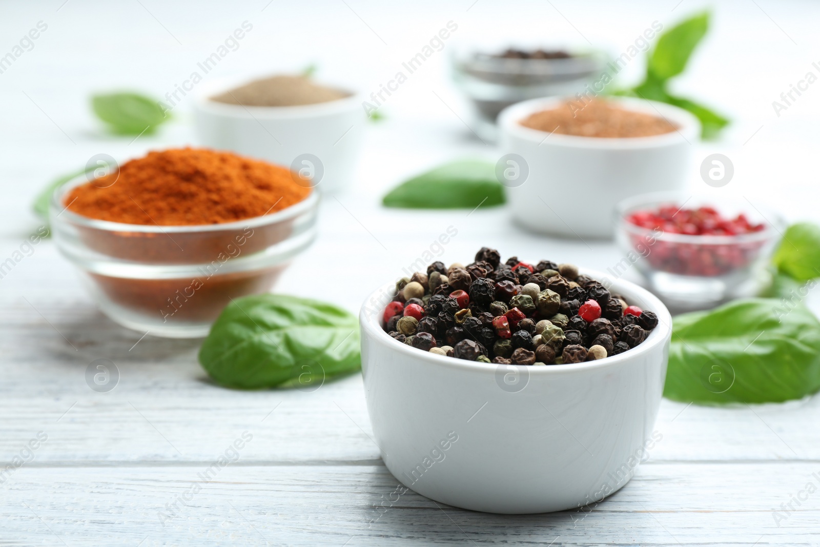 Photo of Bowl of mixed pepper corns on white wooden table, space for text