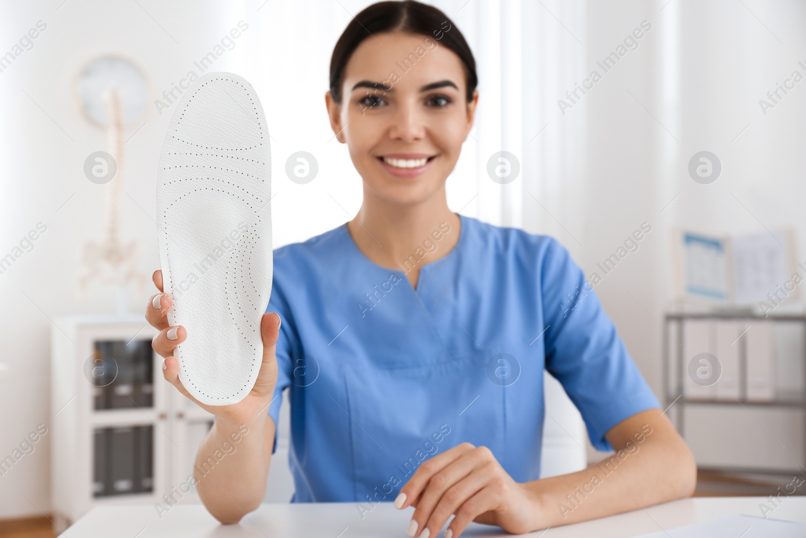 Photo of Young female orthopedist showing insole in clinic