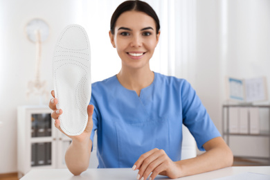 Young female orthopedist showing insole in clinic