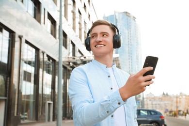 Photo of Handsome man in headphones with smartphone outdoors