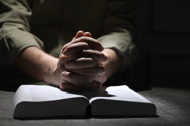 Religion. Christian man praying over Bible at table, closeup