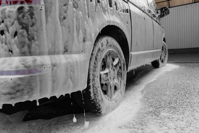 Photo of Modern automobile covered with foam at car wash, closeup