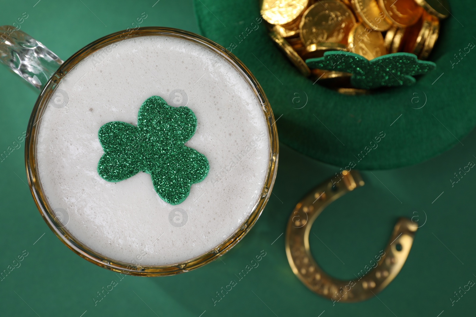 Photo of St. Patrick's day party. Green beer, leprechaun hat with gold, horseshoe and decorative clover leaves on green background, flat lay