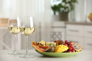 Delicious exotic fruits and glasses of wine on white table indoors