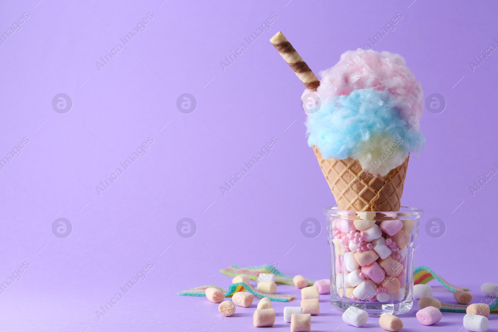 Photo of Sweet cotton candy in waffle cone and marshmallows on purple background, closeup. Space for text