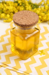 Rapeseed oil in glass bottle and beautiful yellow flowers on table, closeup