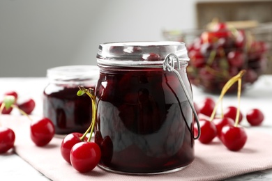 Photo of Jars of pickled cherries and fresh fruits on table