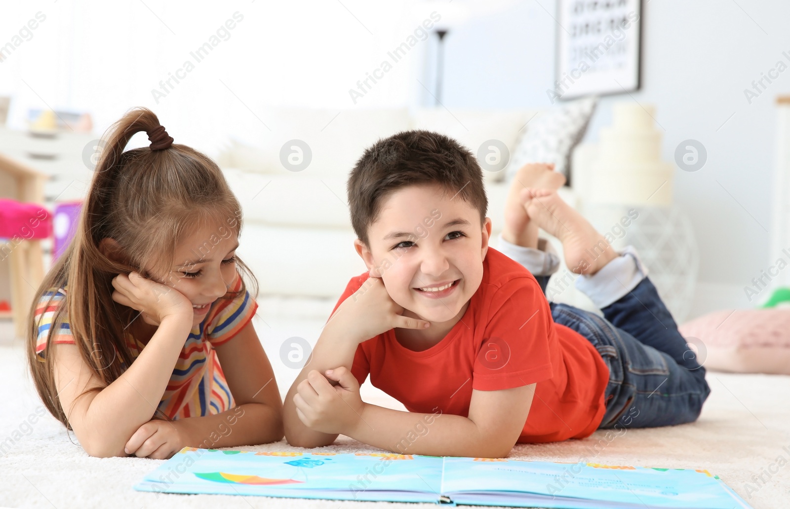 Photo of Cute little children reading book on floor in playing room