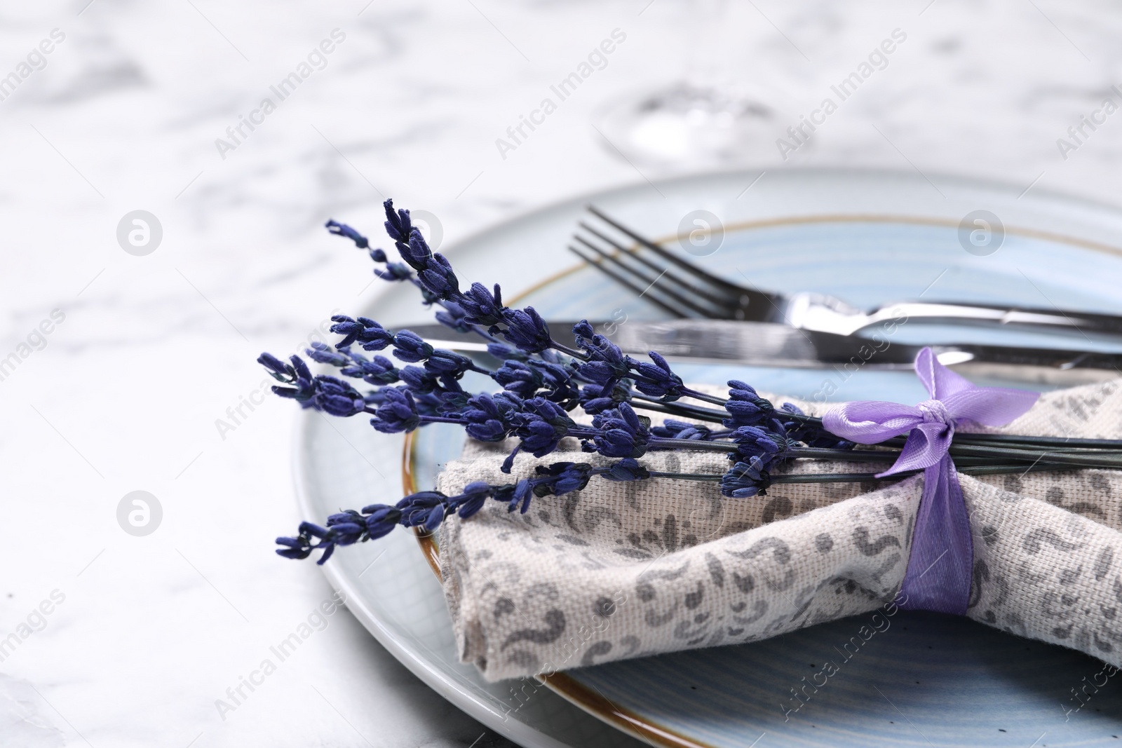 Photo of Cutlery, napkin, plates and preserved lavender flowers on white marble table, closeup. Space for text