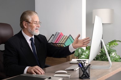 Happy senior boss having online meeting via computer at wooden table in office