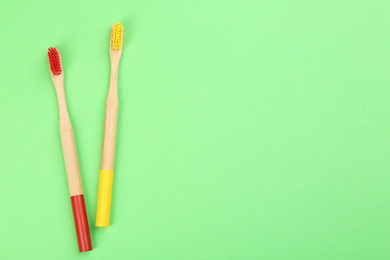 Photo of Natural bamboo toothbrushes on green background, flat lay. Space for text