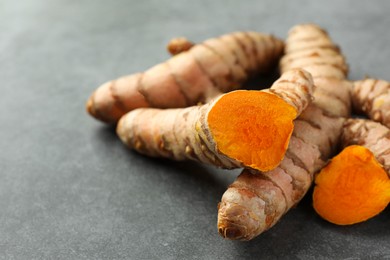 Whole and cut turmeric roots on grey table, closeup. Space for text