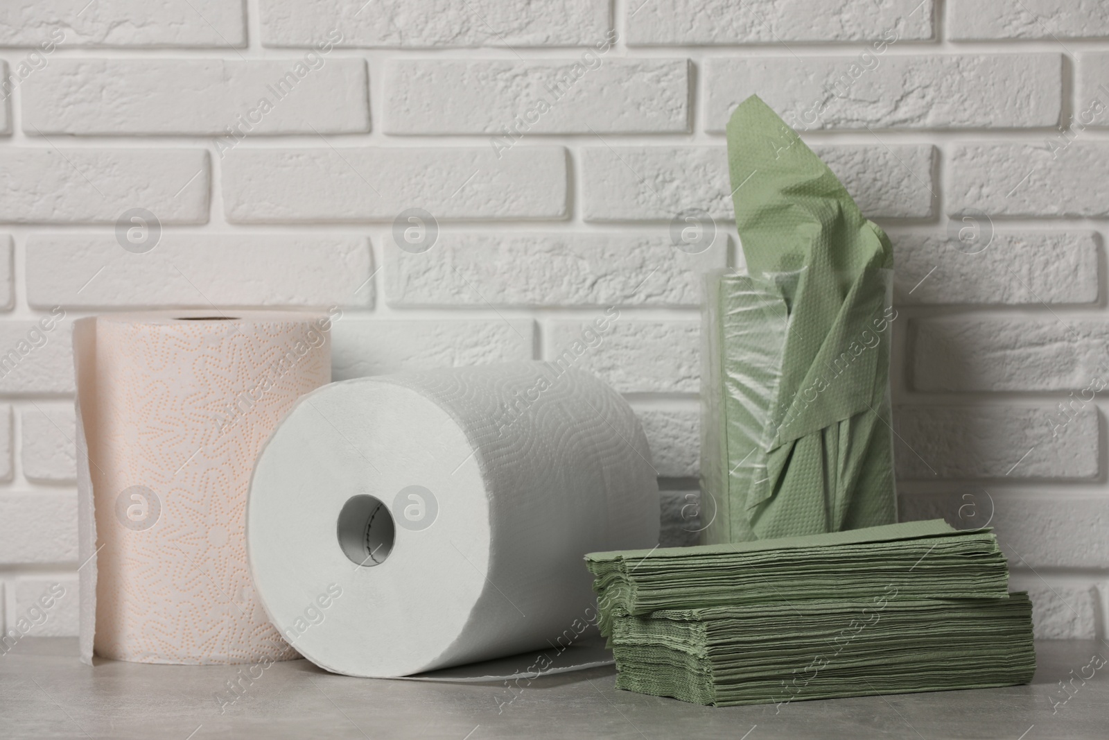 Photo of Different paper towels and napkins on grey table near white brick wall