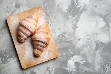 Wooden board with fresh croissants, powdered sugar and space for text on grey table, top view. French pastry