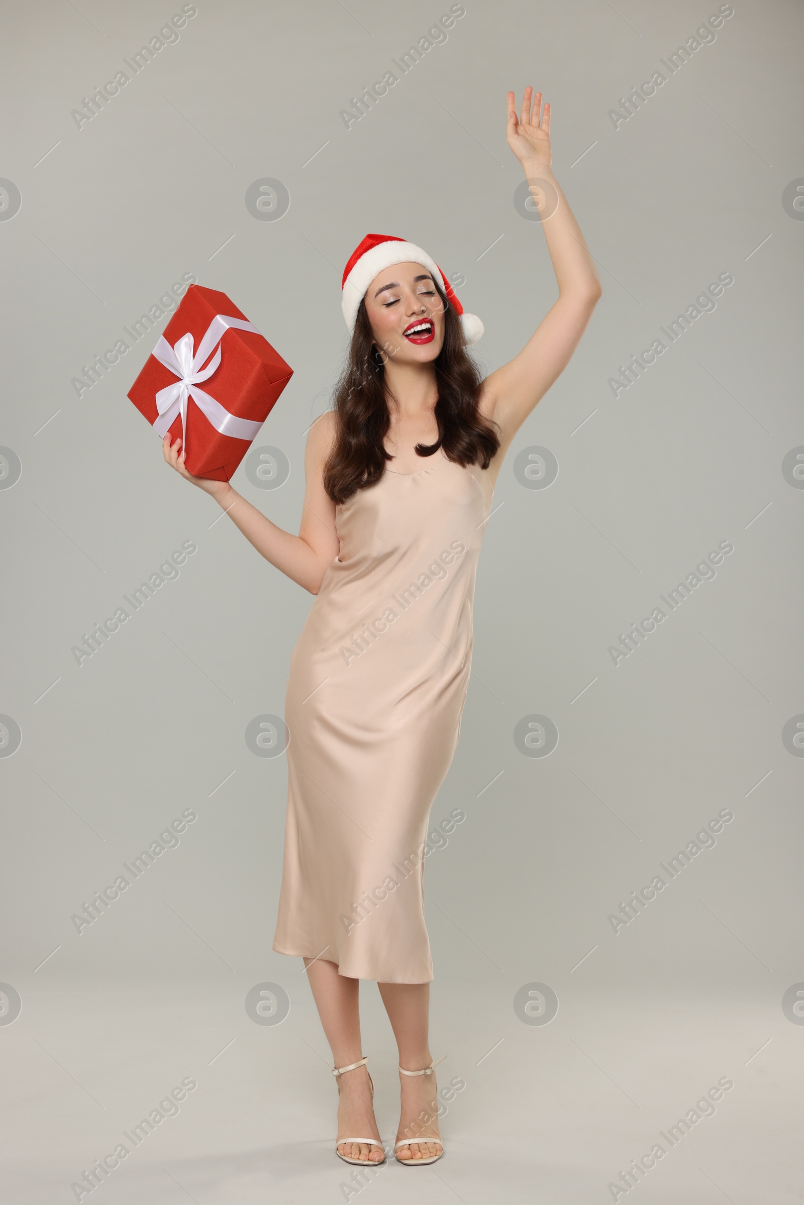 Photo of Beautiful young woman in Santa hat with Christmas gift on grey background