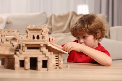 Cute little boy playing with wooden castle at table in room. Child's toy