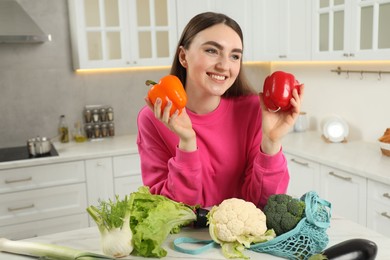 Woman with peppers and string bag of vegetables at light marble table in kitchen