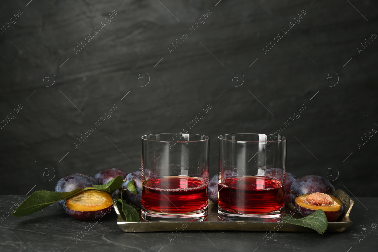 Photo of Delicious plum liquor and ripe fruits on black table. Homemade strong alcoholic beverage