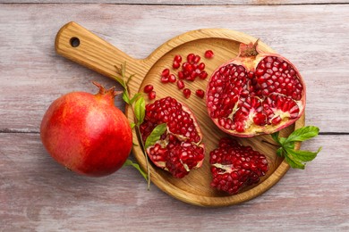 Fresh pomegranates and green leaves on wooden table, top view