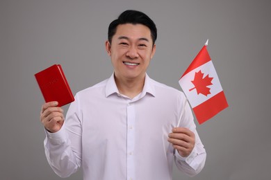 Immigration. Happy man with passport and flag of Canada on grey background