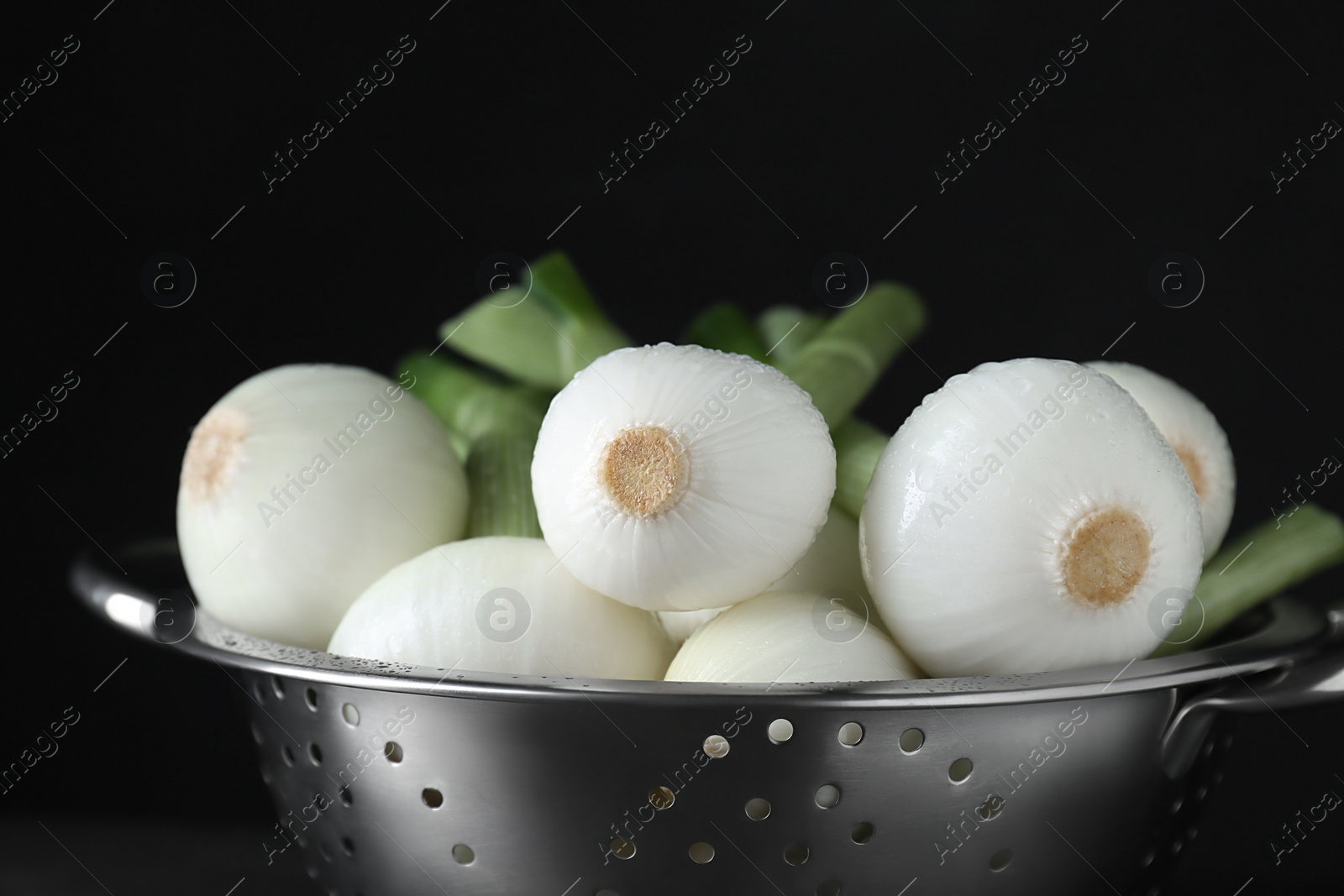 Photo of Colander with green spring onions on black background, closeup