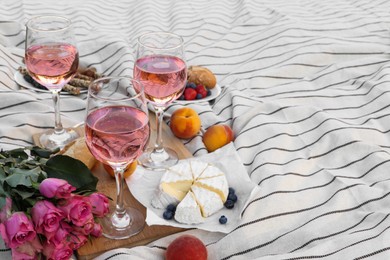 Photo of Glasses of delicious rose wine, flowers and food on white picnic blanket, space for text