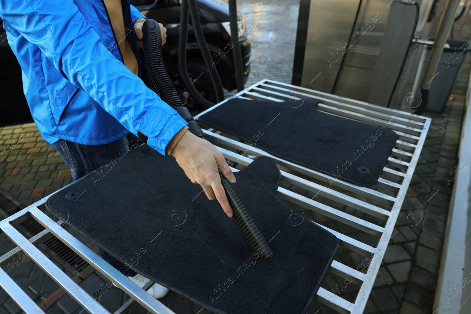 Photo of Man cleaning auto carpets with vacuum cleaner at self-service car wash, closeup