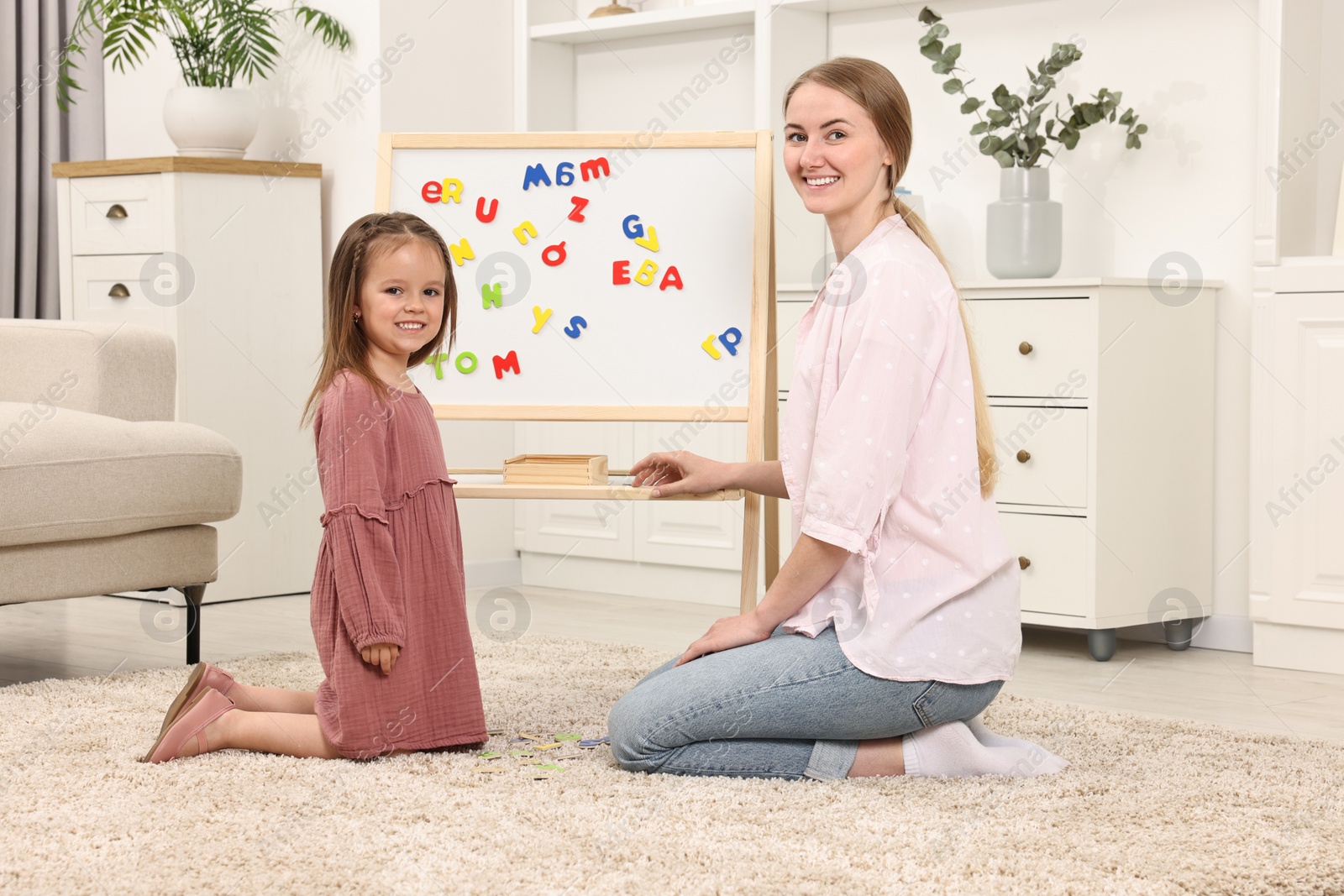 Photo of Mom teaching her daughter alphabet with magnetic letters at home