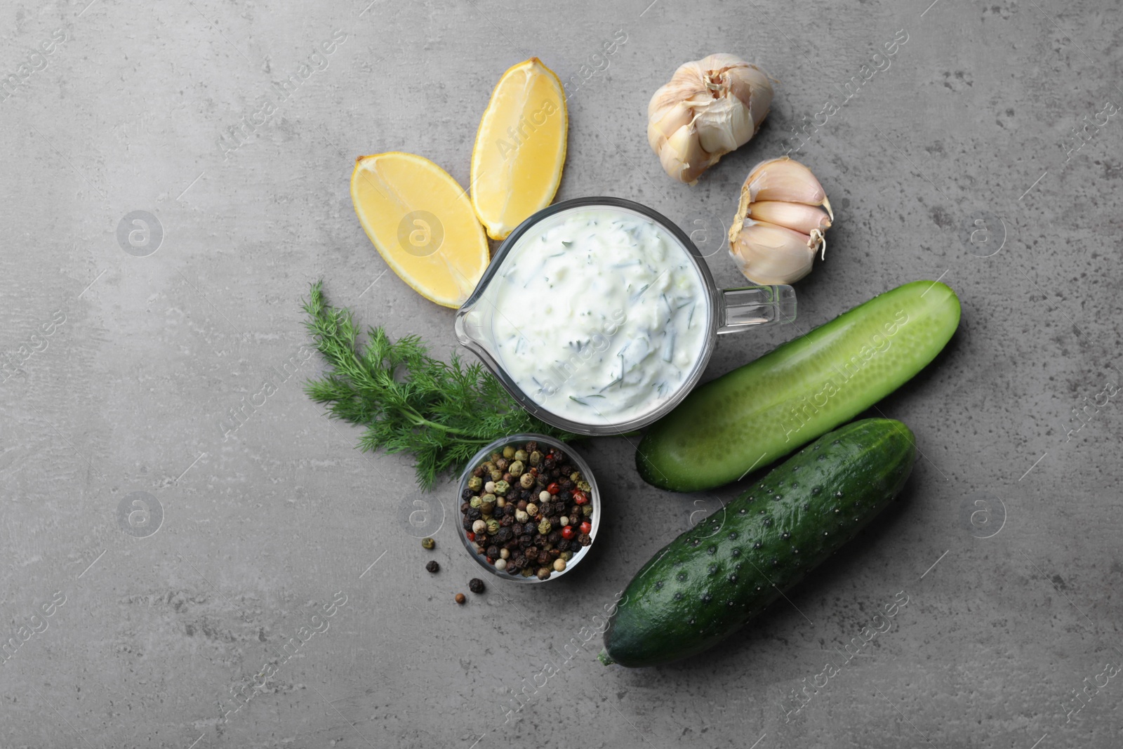 Photo of Tzatziki cucumber sauce with ingredients on grey background, flat lay