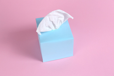 Box with paper tissues on pink background