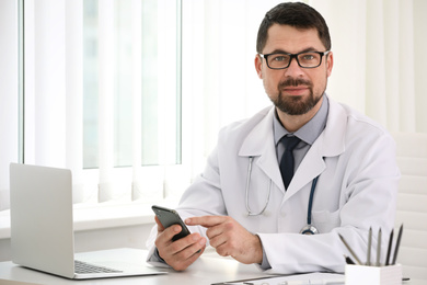 Male doctor with smartphone at table in office