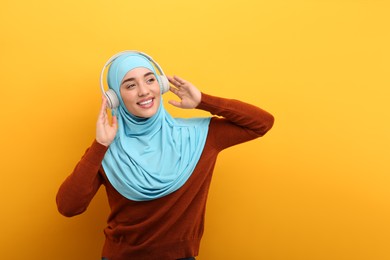 Photo of Muslim woman in hijab and headphones listening to music on orange background, space for text