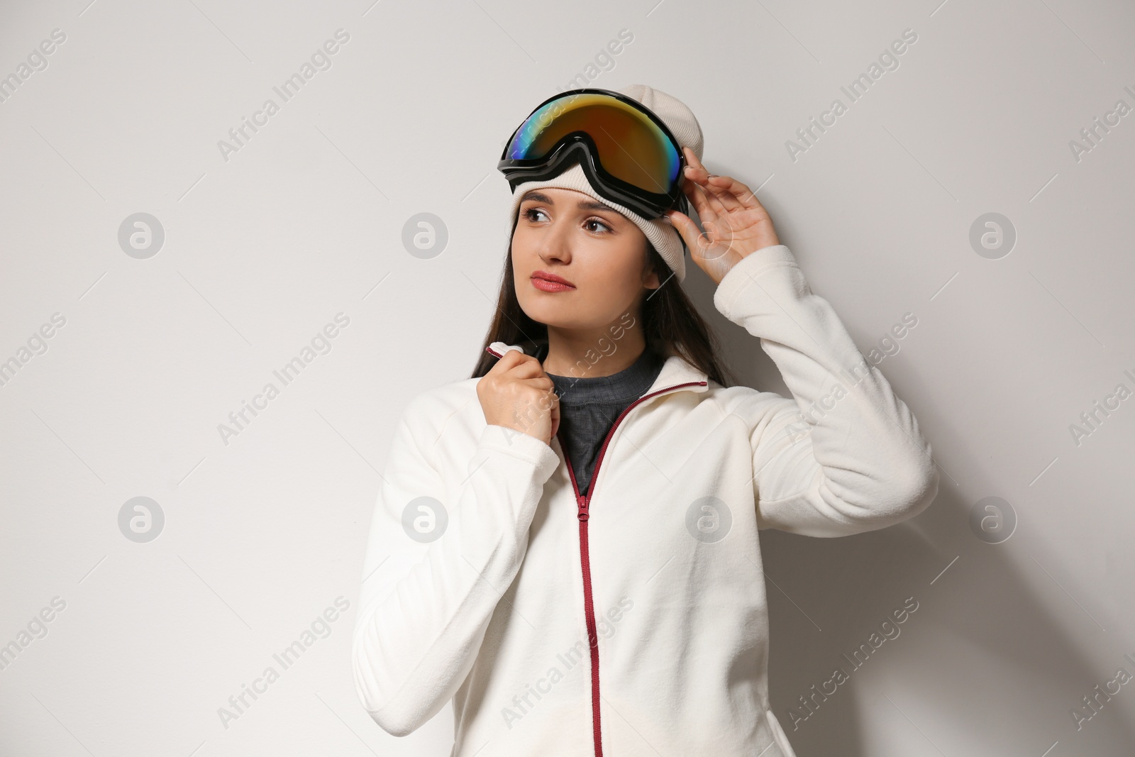 Photo of Woman wearing fleece jacket and goggles on light grey background. Winter sport clothes