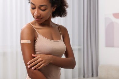 Photo of Young woman with adhesive bandage on her arm after vaccination indoors. Space for text