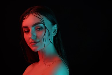Photo of Portrait of beautiful woman in neon lights against black background. Space for text