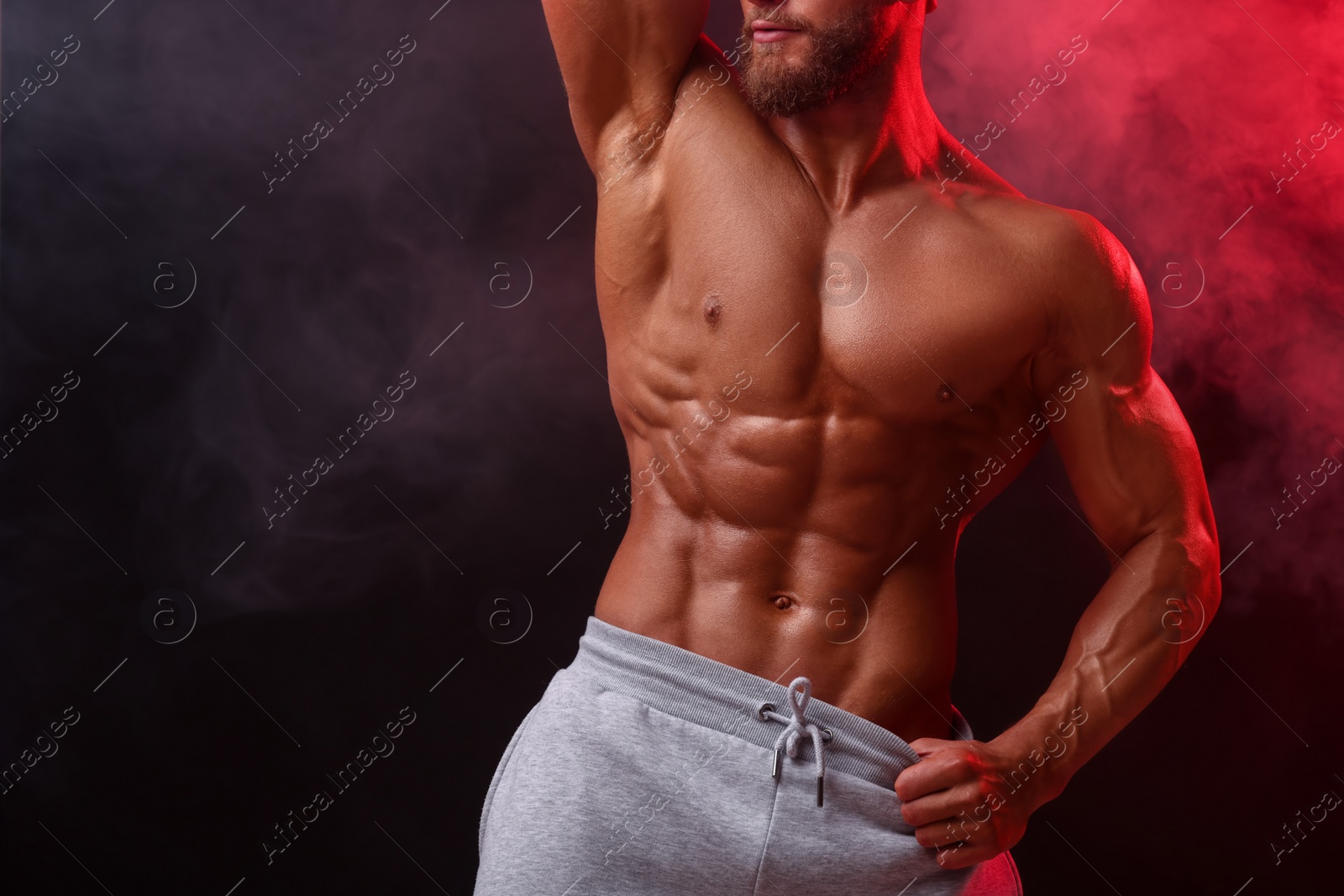 Photo of Young bodybuilder with muscular body in smoke on color background, closeup. Space for text