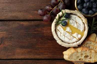 Tasty baked brie cheese and products on wooden table, flat lay. Space for text