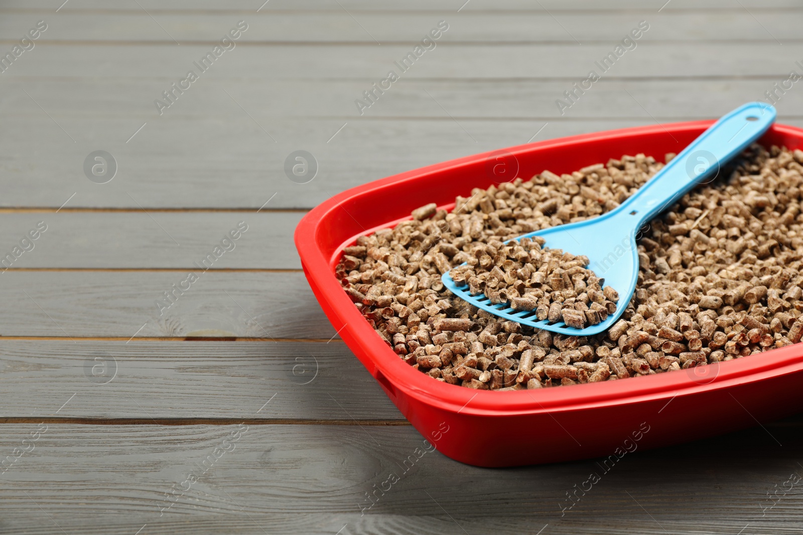 Photo of Cat litter tray with filler and scoop on grey wooden floor, closeup. Space for text