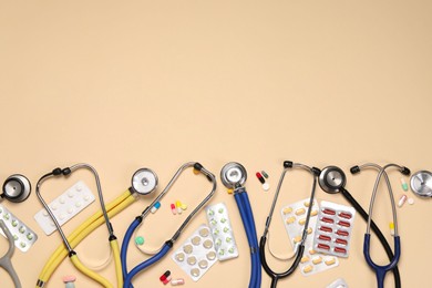 Stethoscopes and pills on beige background, flat lay. Space for text