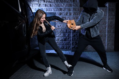 Photo of Woman fighting with thief while he trying to steal her bag near van at night. Self defense concept