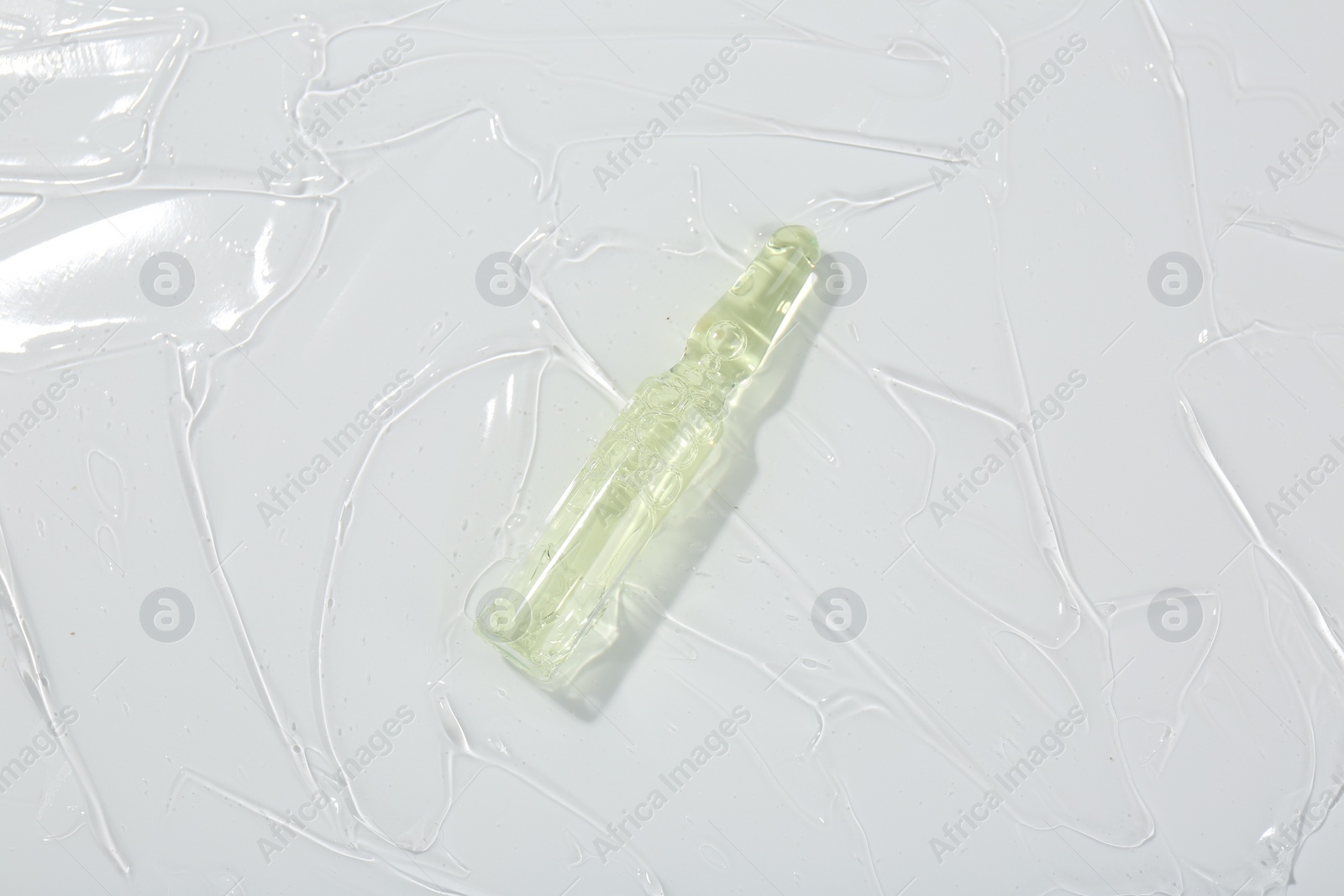 Photo of Skincare ampoule on white surface covered with gel, top view