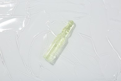 Photo of Skincare ampoule on white surface covered with gel, top view